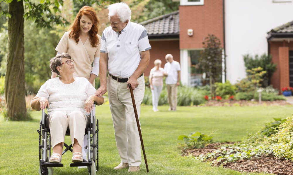 An elderly disabled couple with their caretaker in the garden outside of a private rehabilitation clinic.